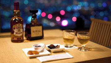 A table with a bottle of whiskey, a bottle of cognac, a glass of whiskey, a glass of water, and a plate with pastries.