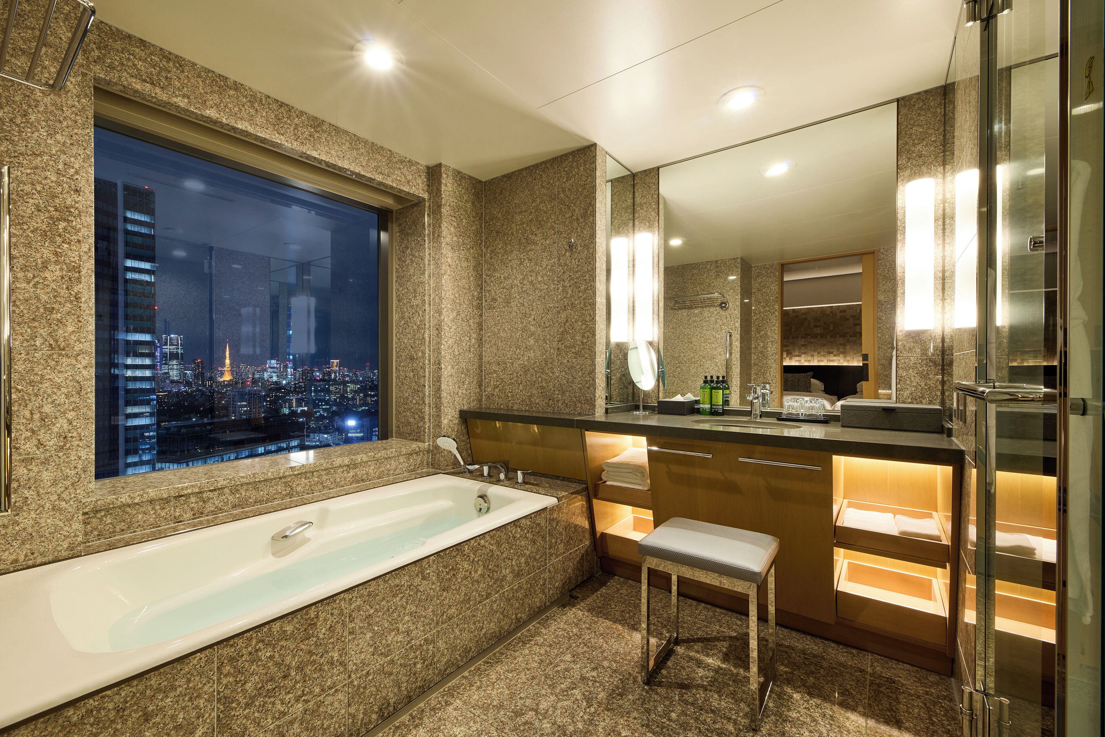 Une salle de bain moderne avec une grande baignoire, un meuble-lavabo avec un miroir et une vue sur le paysage urbain la nuit.