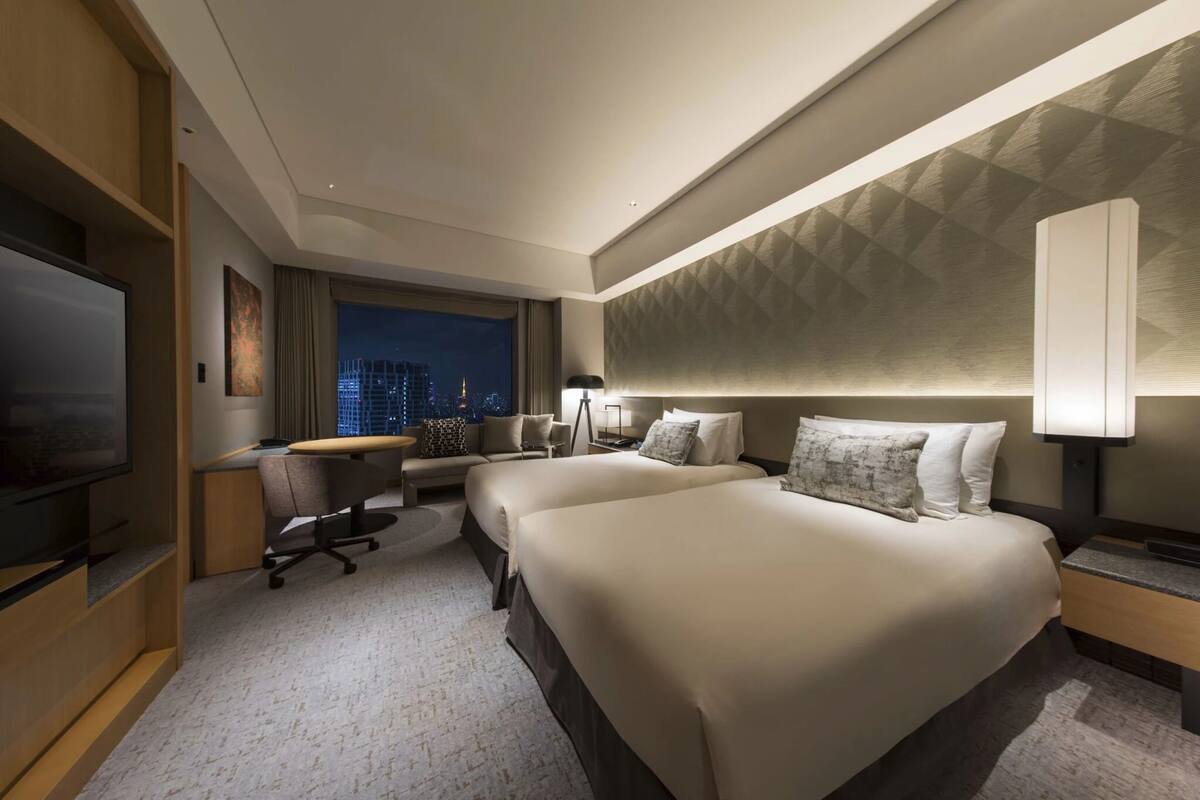 A hotel room with a large bed, a desk, a chair, a TV, and a city view.