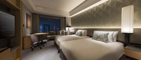 Habitación de hotel con una cama grande, un escritorio, una silla, un televisor y vista a la ciudad.