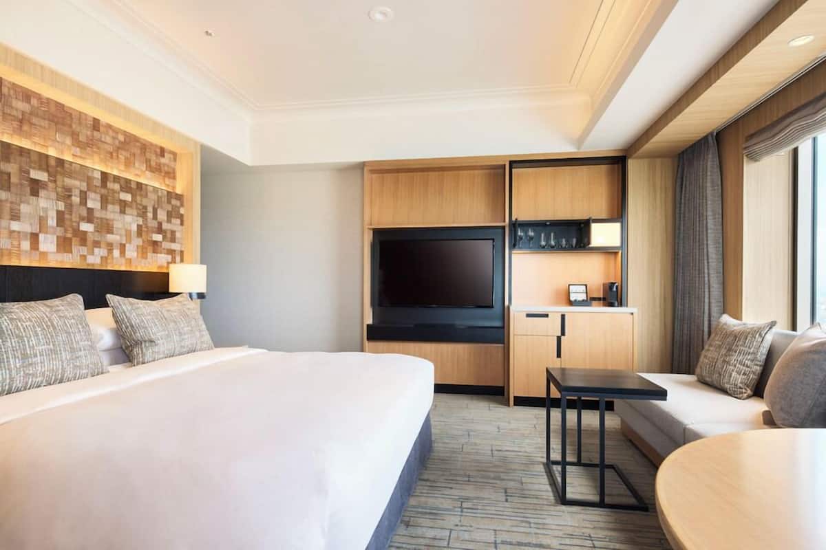A hotel room with a large bed, a flat-screen TV, a kitchenette, and a seating area with a sofa and a small table.