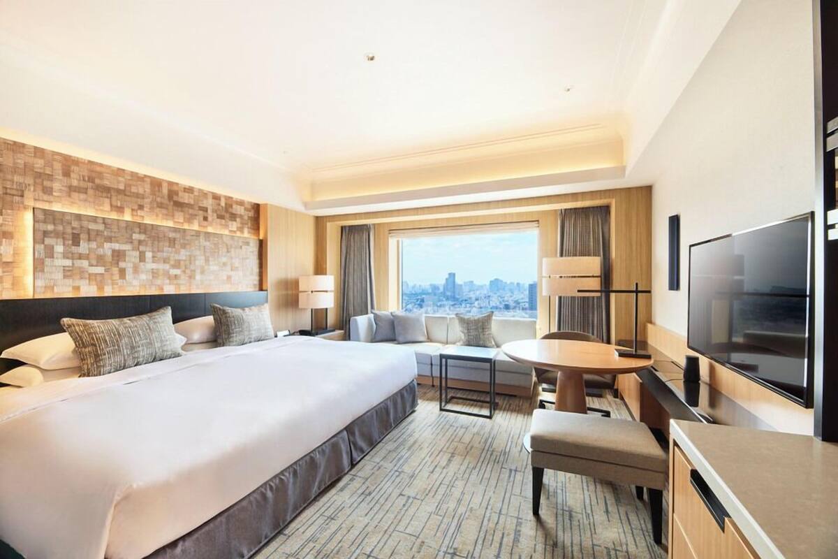A hotel room with a large bed, a desk, a chair, a TV, and a city view.