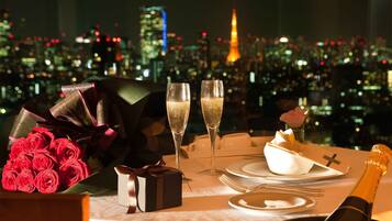 Ein romantisches Dinner mit Rosenblumen, Champagner und einer Geschenkschachtel auf einem Tisch, im Hintergrund ist die Stadt zu sehen.