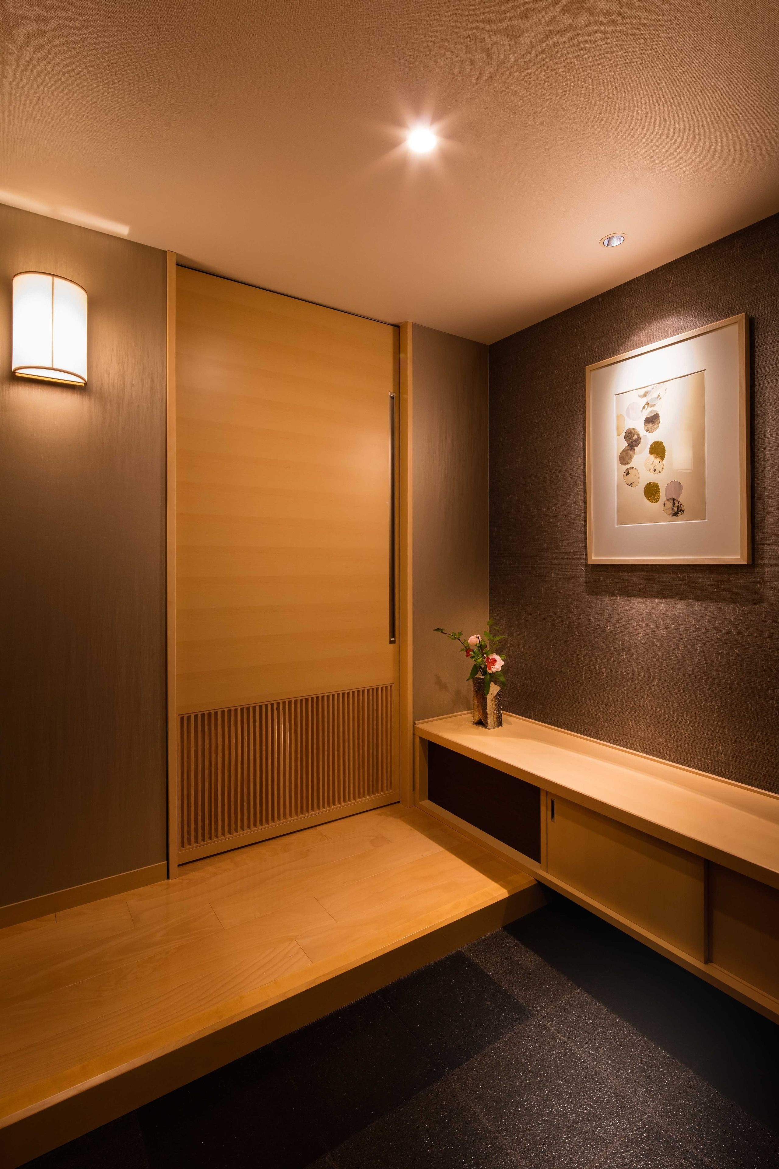 A modern hotel lobby with a wooden bench, a wall-mounted light, and a framed artwork.