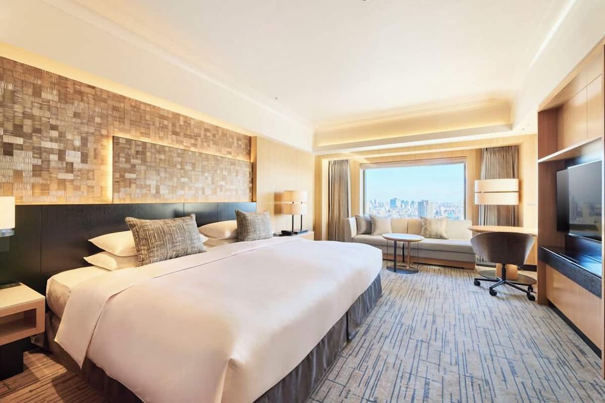 A hotel room with a large bed, a city view, a TV, and a seating area with a table and chairs.