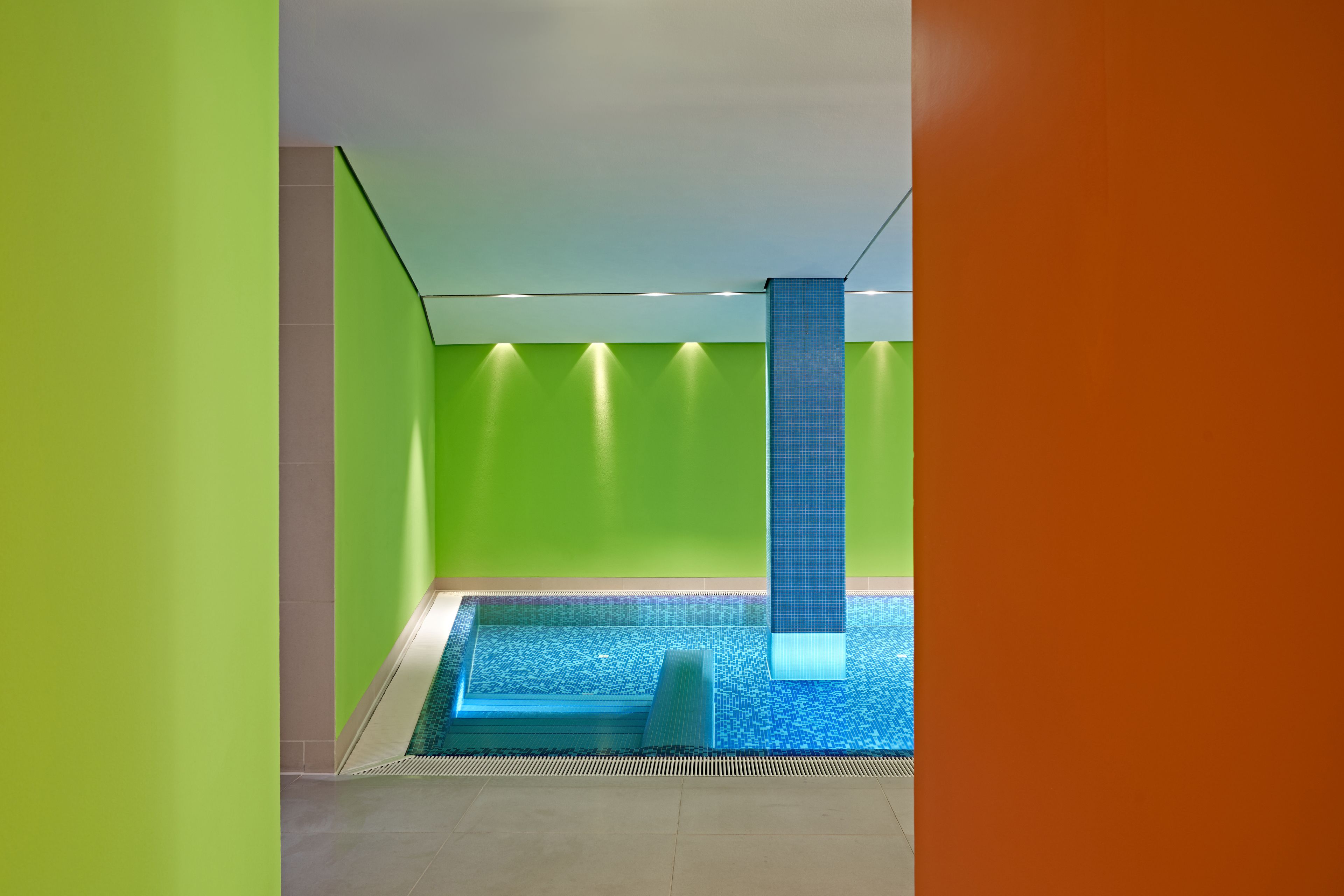 Area piscina interna moderna, con pareti verdi e pavimento in piastrelle blu.