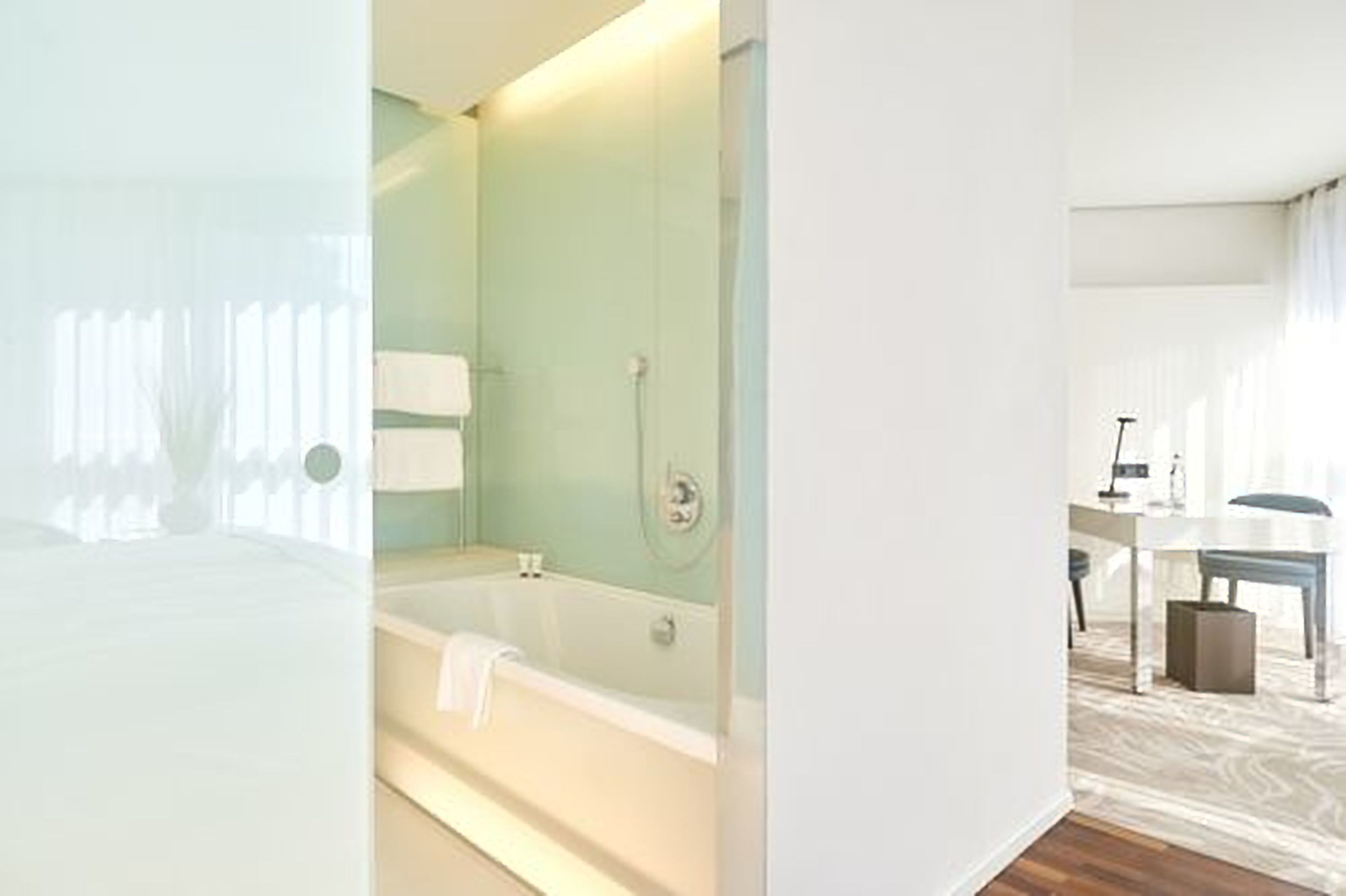 Una habitación de hotel moderna con una cama grande, un baño independiente con bañera, y un escritorio con silla y lámpara.
