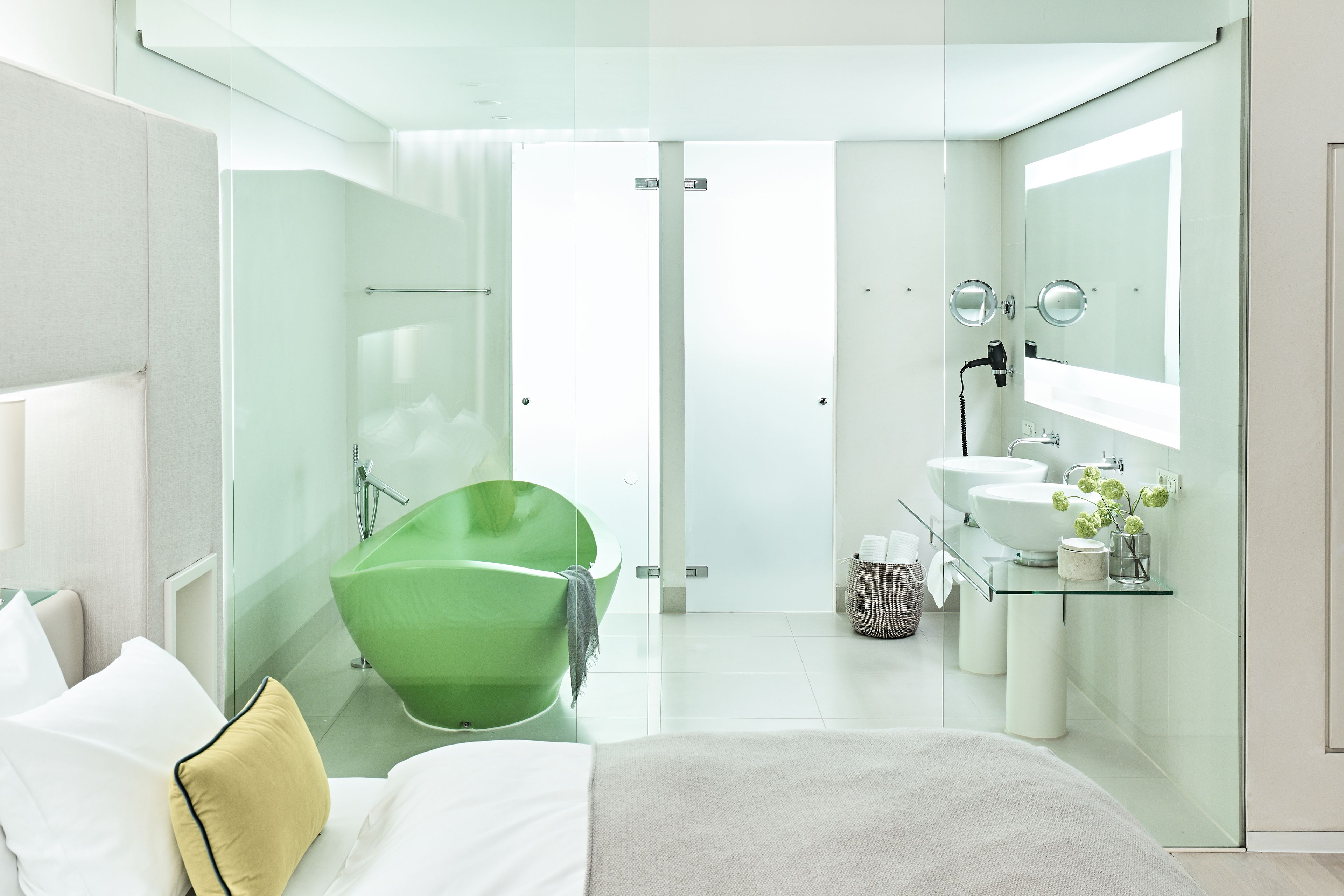 Un baño moderno con ducha envuelta en cristal, una bañera verde y un lavabo doble.