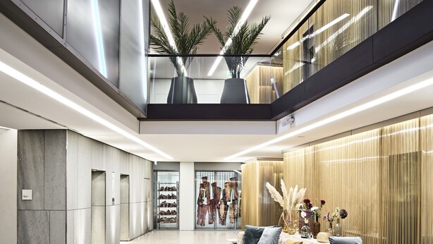 Un interior moderno con una zona de estar central, una exhibición de zapatos y una planta en el nivel superior.
