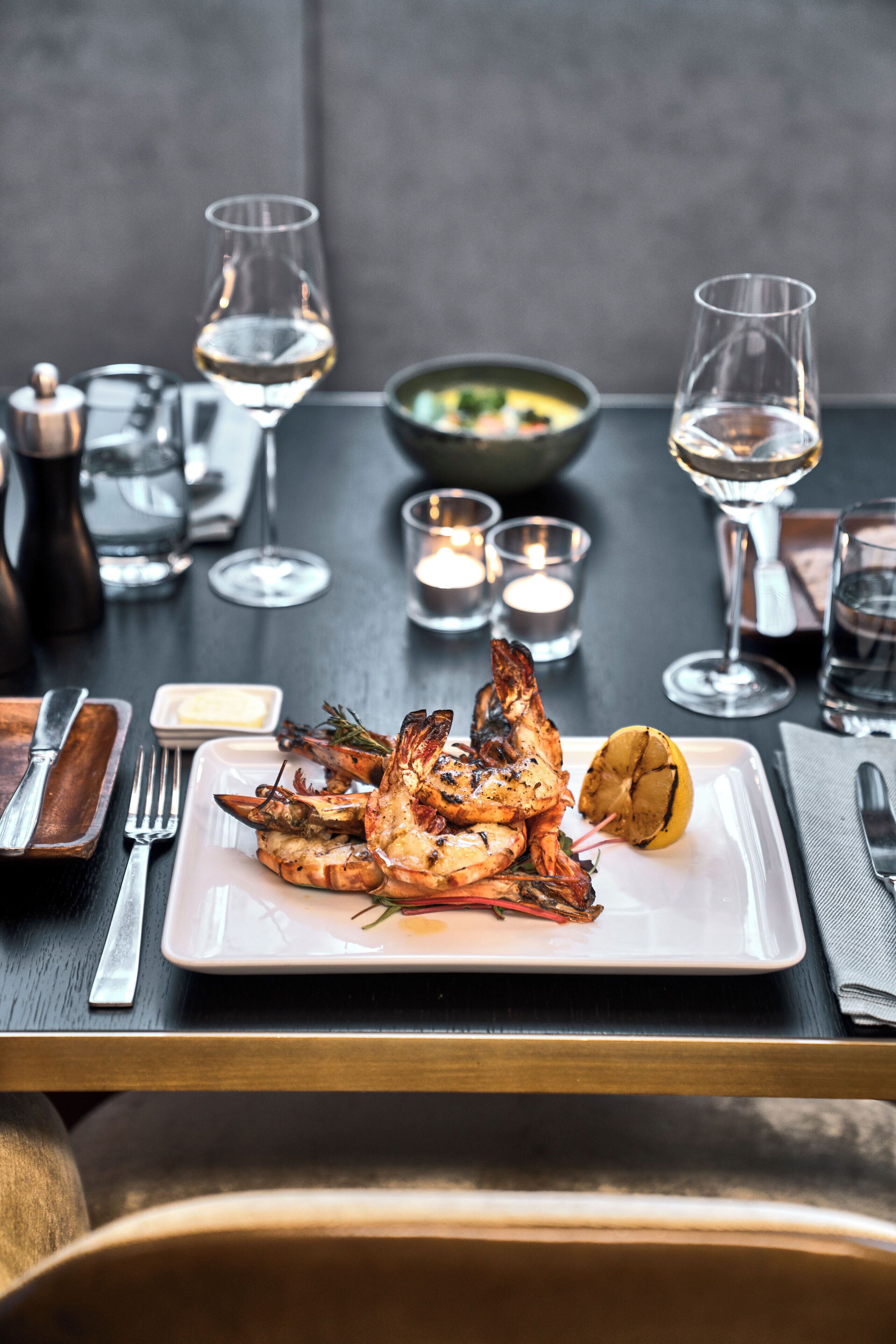 A dining table with a plate of grilled shrimp, a bowl of salad, and several glasses of white wine.