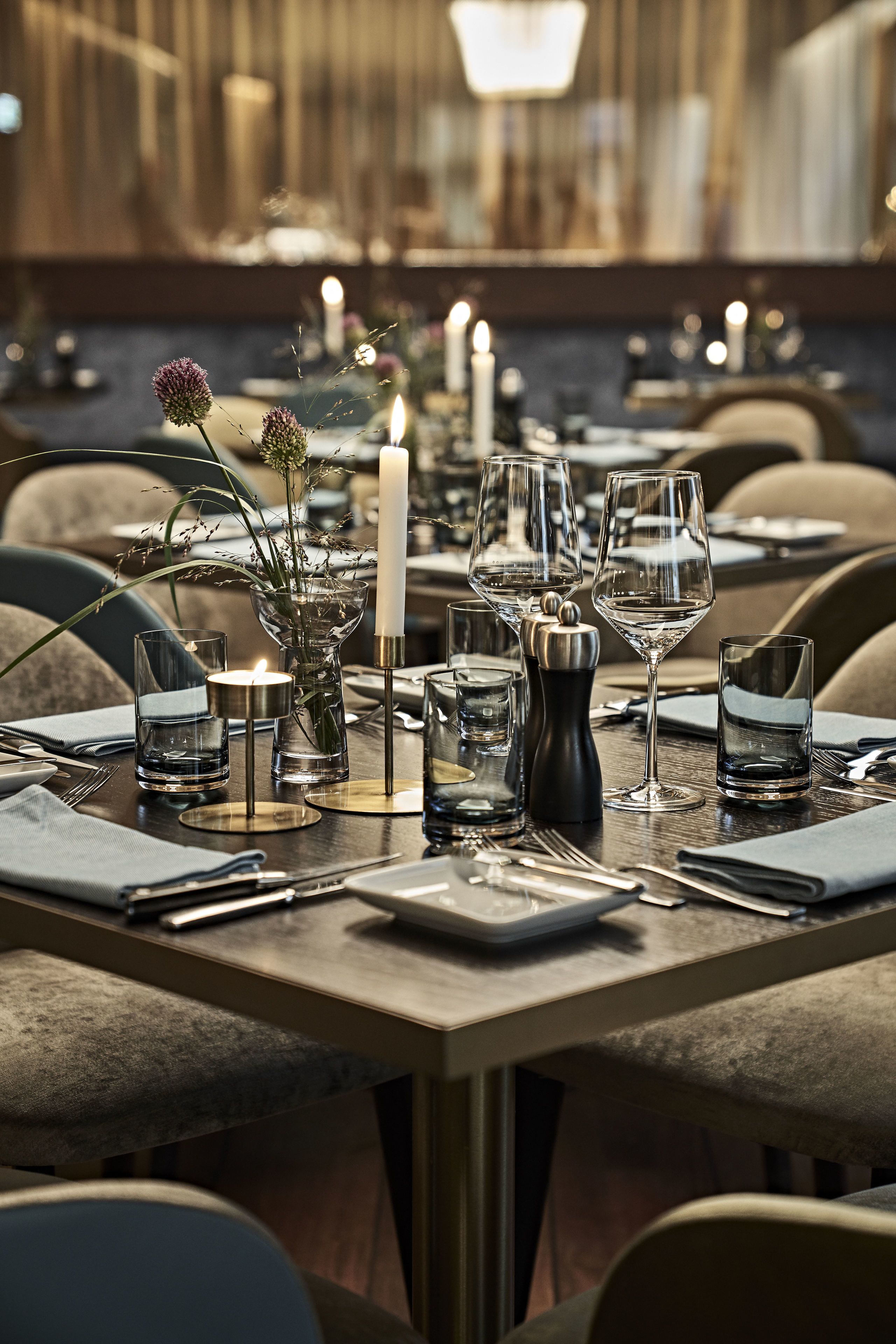 A dining table set with wine glasses, a candle, and a vase with flowers.