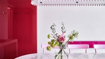 Ein Marmortisch mit einer klaren Vase, die Blumen enthält, rosafarbene Stühle und eine rote Wand.