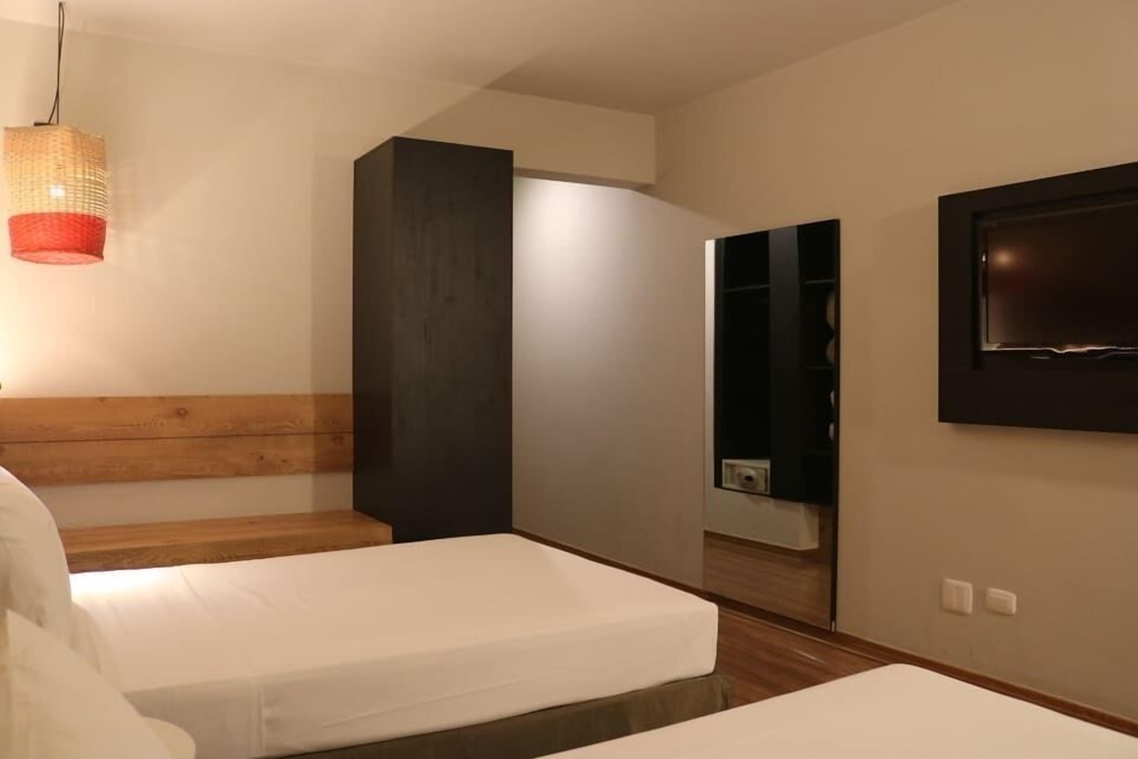 Una camera da letto moderna con due letti, una testata imbottita in legno, uno specchio grande e una TV fissata al muro.