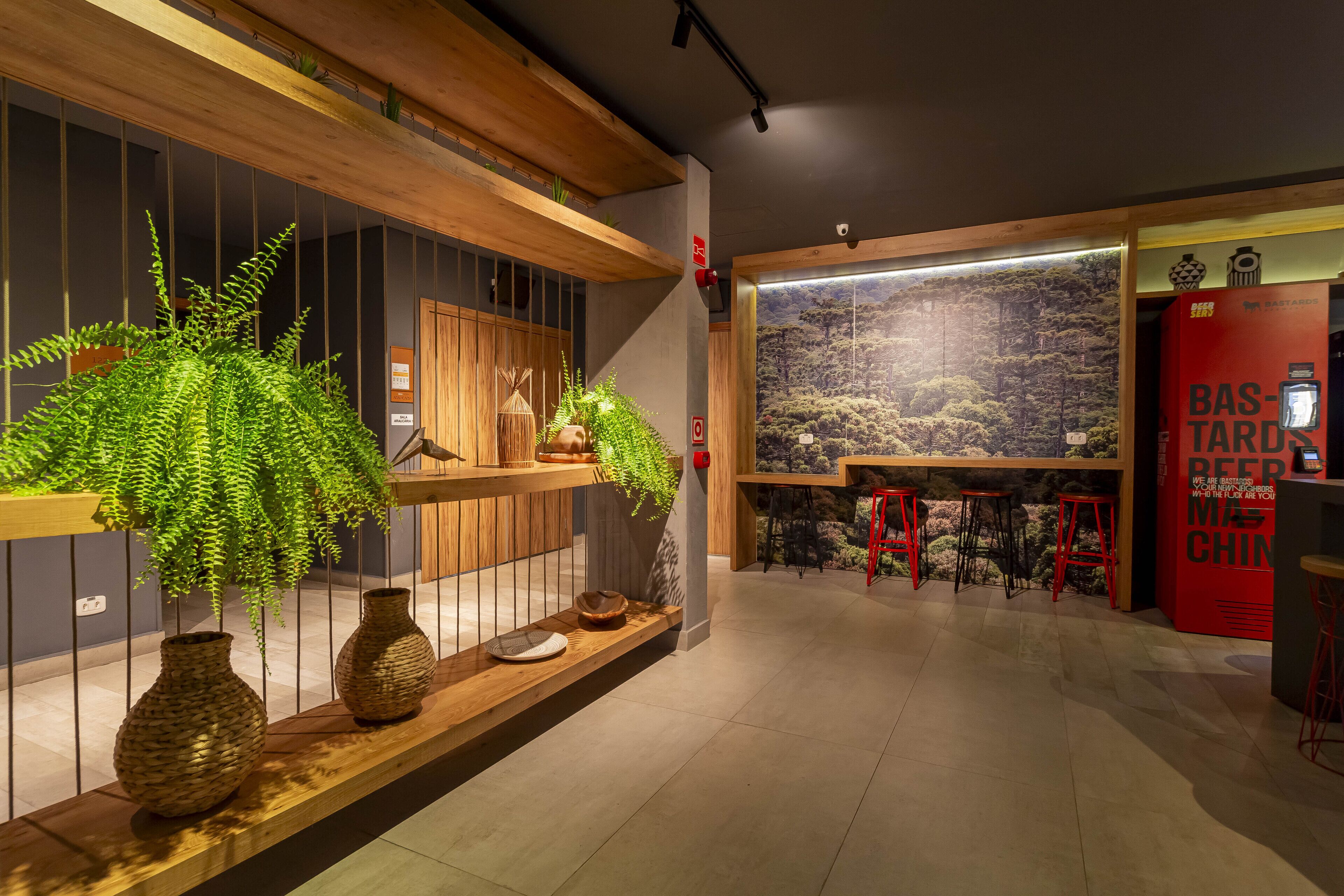 A modern bar area with wooden shelves, potted plants, and red bar stools.