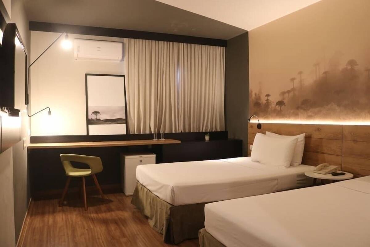 Una habitació d'hotel amb dos llits, un escriptori, una cadira, aire condicionat i un quadre a la paret.