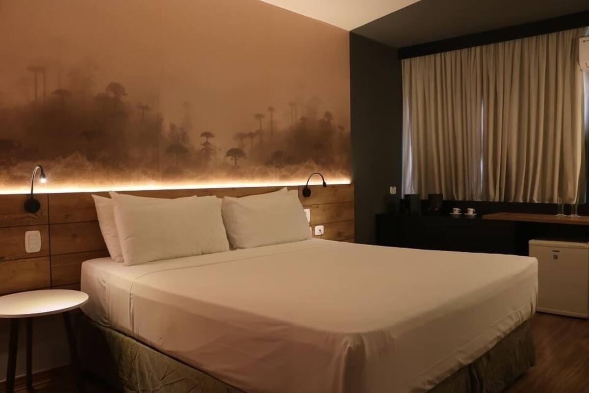 Habitació d'hotel amb un llit, una taula petita, una tauleta de nit i una làmpada fixada a la paret.