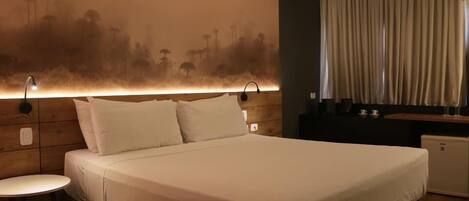 Una habitación de hotel con una cama, una mesita, una mesita de noche y una lámpara de pared.