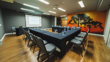 Uma sala de conferências com uma mesa comprida, cadeiras, uma tela de projetor e um mural na parede.