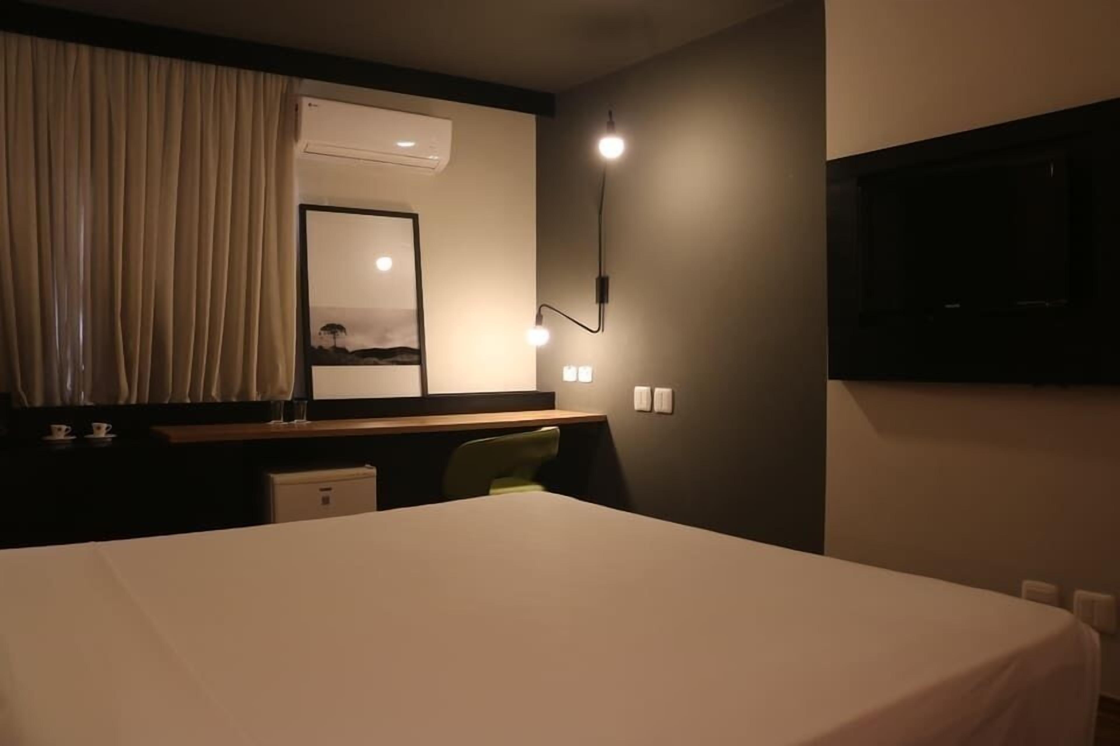 A hotel room with a bed, a desk with a chair, a mirror, and a TV mounted on the wall.