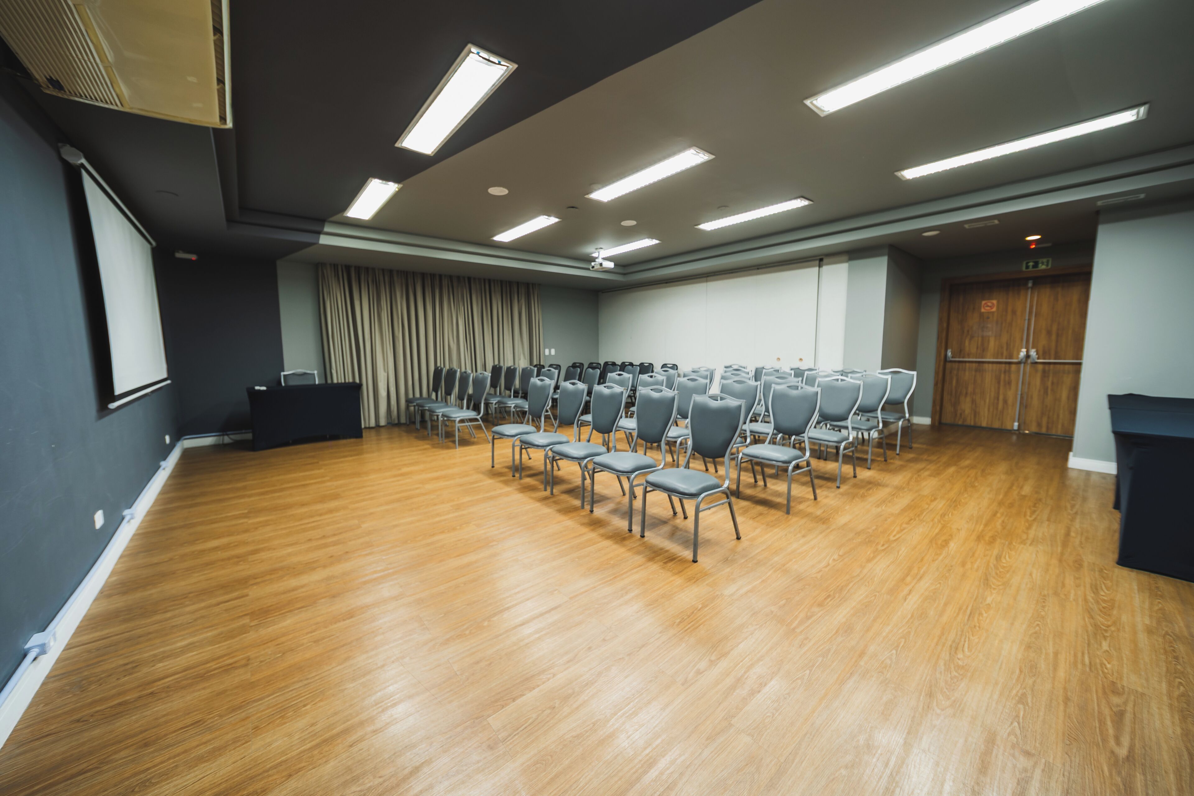 A conference room with rows of chairs, a podium, and a projector screen.