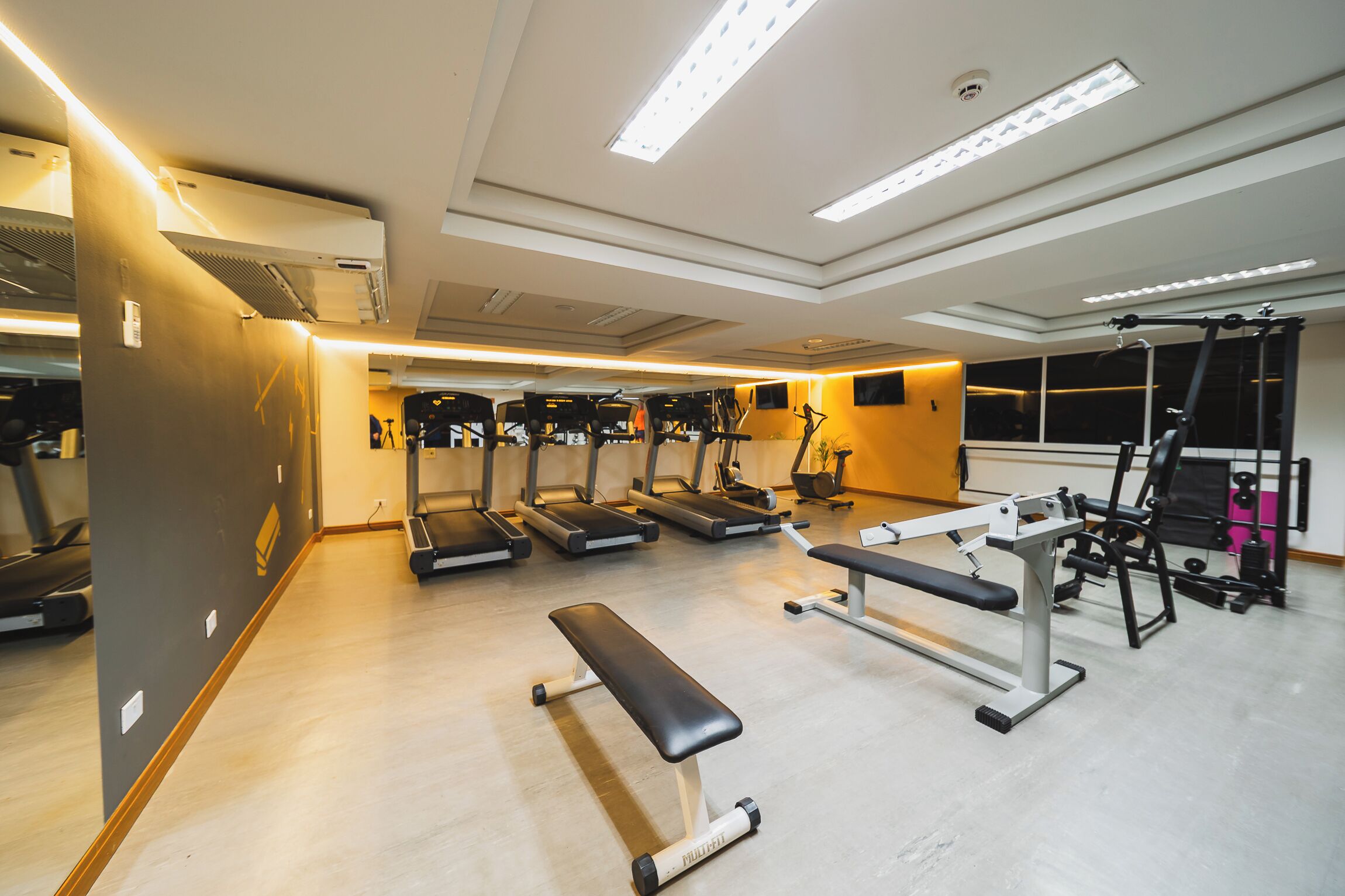 Un gimnasio con cintas de correr, una banca y máquinas de pesas.