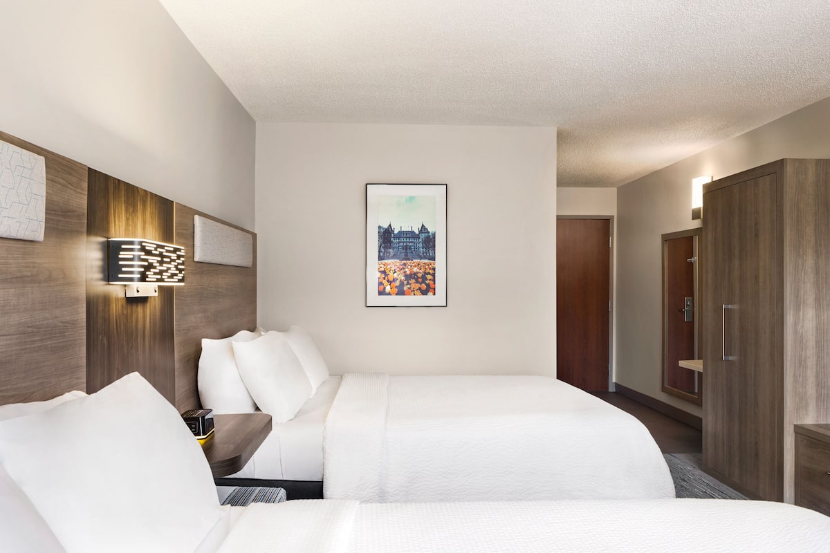 Ein Hotelzimmer mit zwei Betten, einem hölzernen Kopfteil, einer Wandleuchte und einem gerahmten Bild.