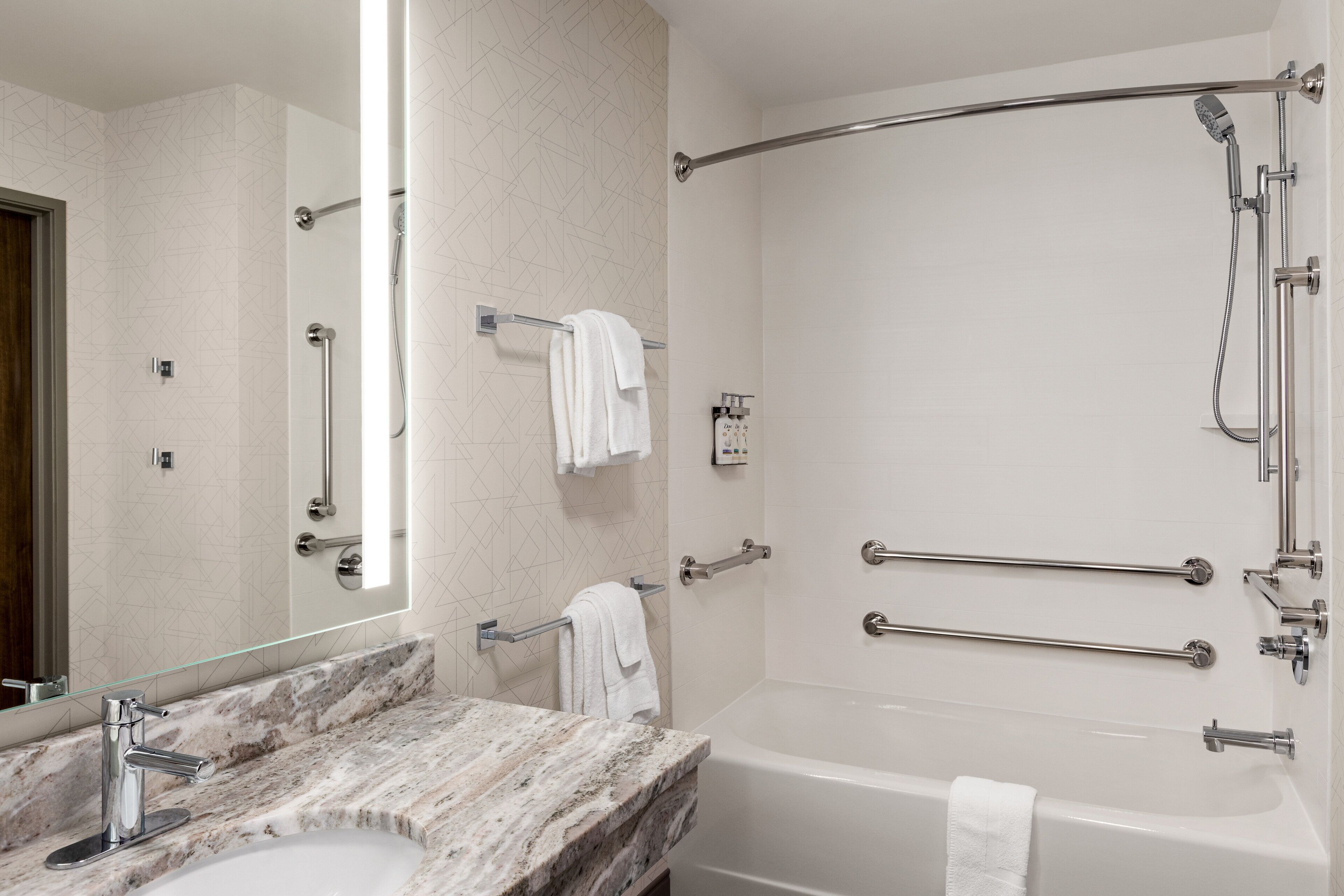 Un baño moderno con lavamanos de mármol, bañera y ducha con barras de apoyo.