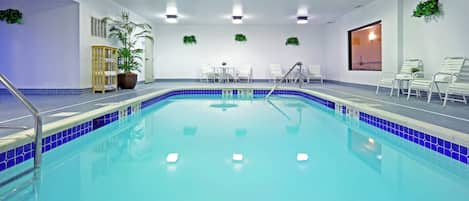 An indoor swimming pool with clear water, a tiled edge, and a few lounge chairs around the perimeter.