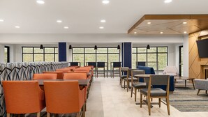 En moderne hotellobby med siddeområder, store vinduer og et fladskærms-tv monteret på væggen.