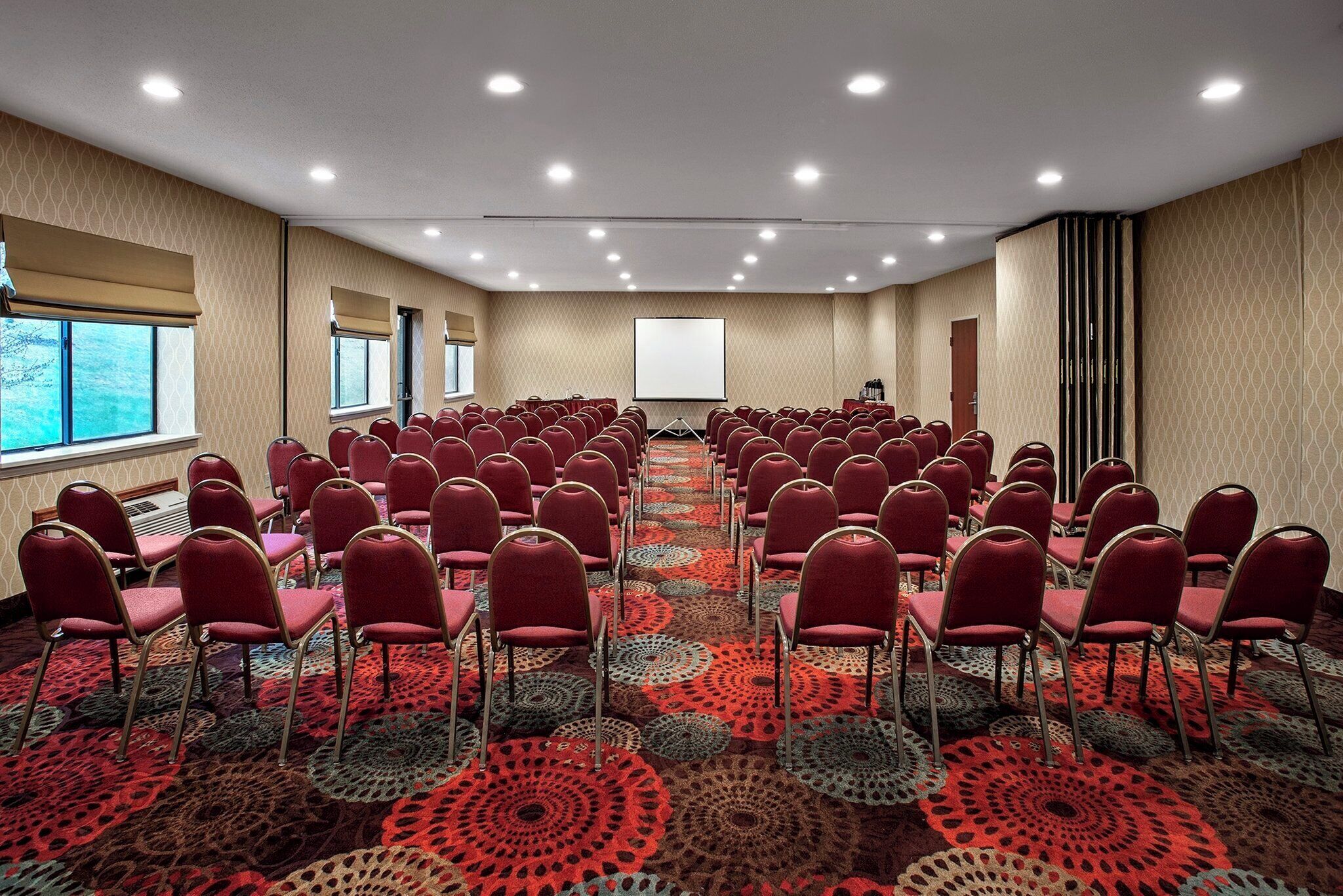 Una sala conferenze con file di sedie rosse, uno schermo per proiettore e una moquette fantasia.