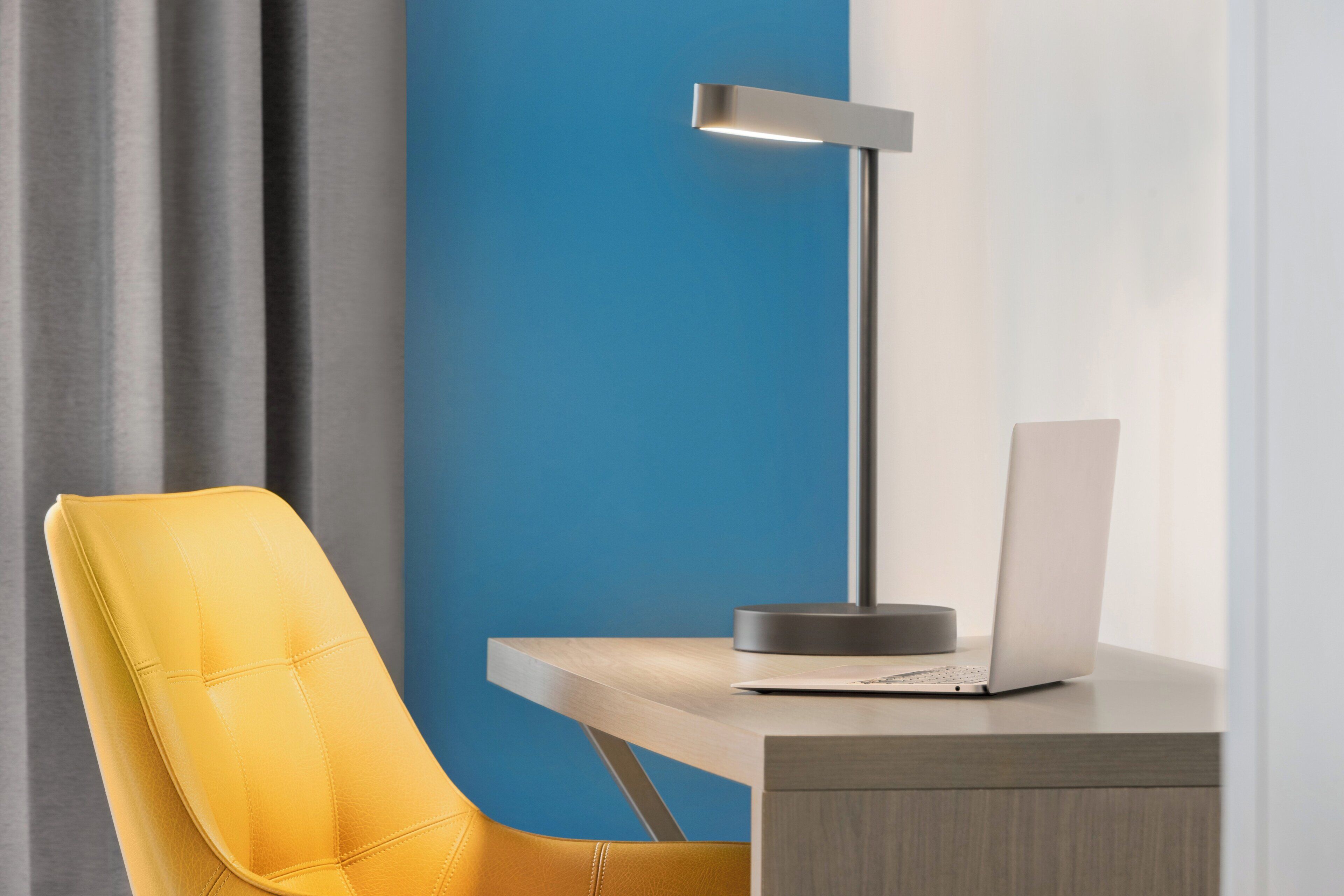 Een moderne bureaustoel, een bureau met een laptop en een vloerlamp.