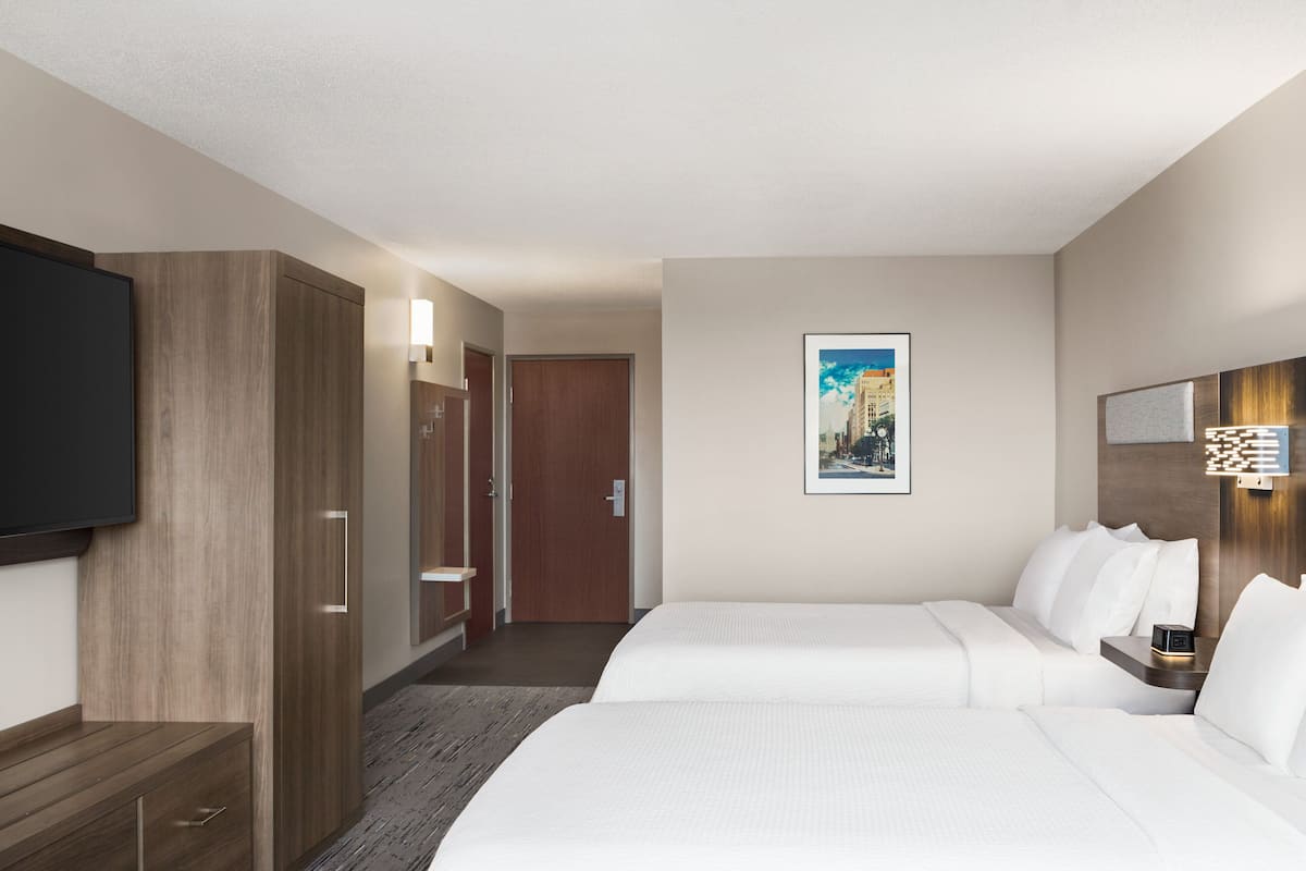 Ein Hotelzimmer mit zwei Betten, einem Fernseher, einem Gemälde und einem Schreibtisch mit Lampe.