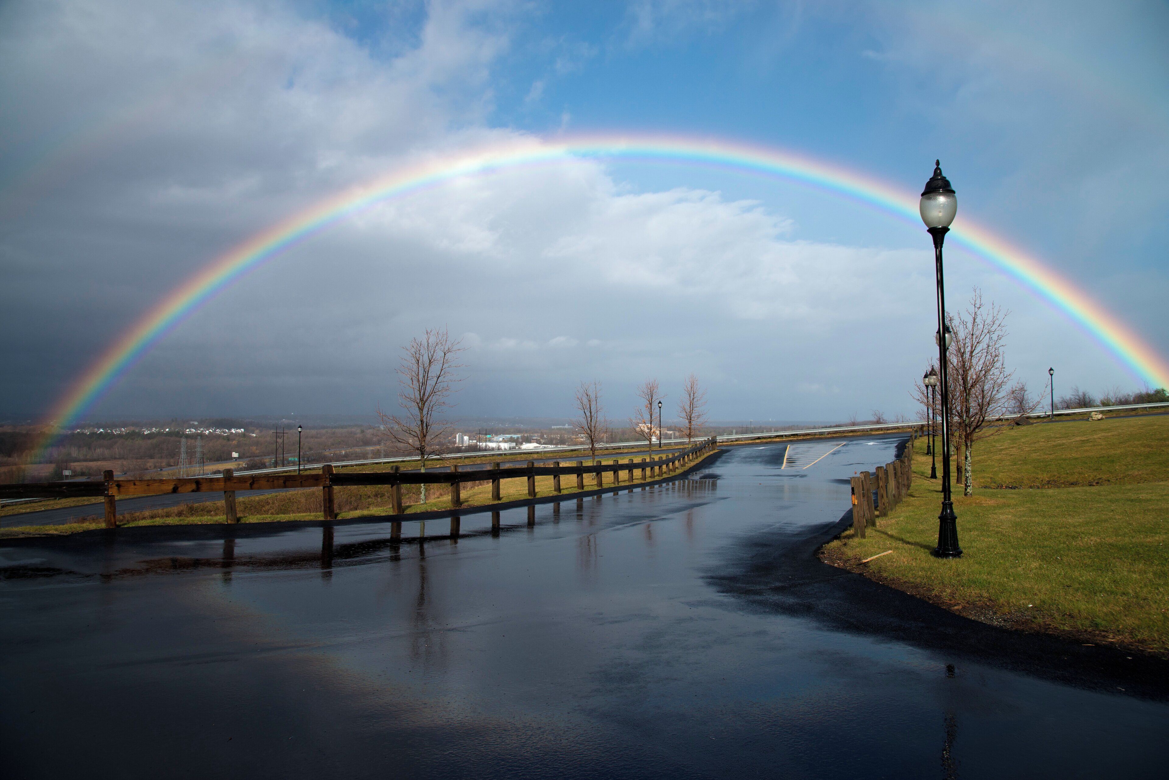Canal pluvial con un arcoíris que se arquea sobre él, rodeado de un área de césped y una cerca.