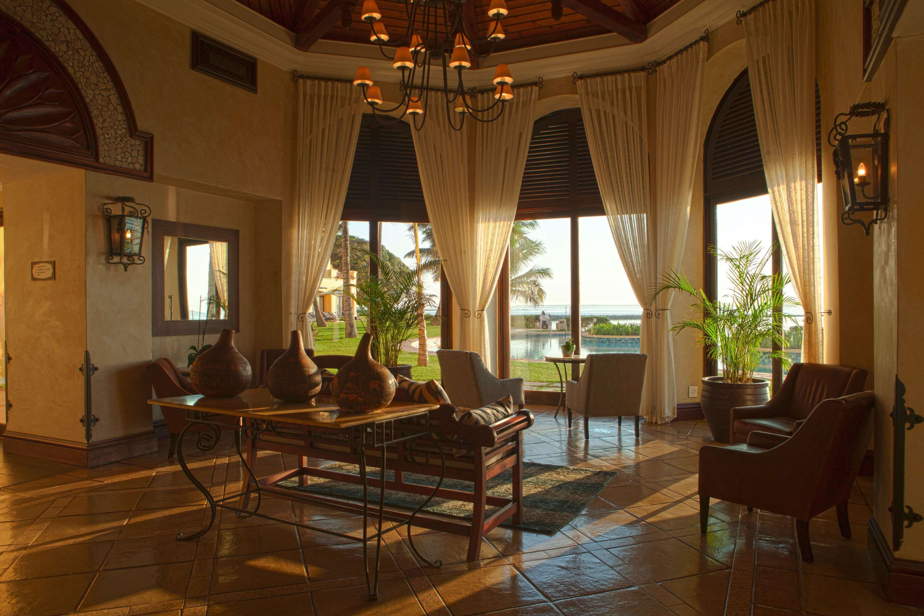 A spacious lobby with a large table, comfortable seating, and large windows offering a view of the outdoors.