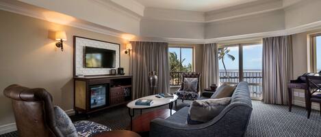 Habitación de hotel con un sofá grande, televisor, mesa de comedor y balcón con vista al océano.