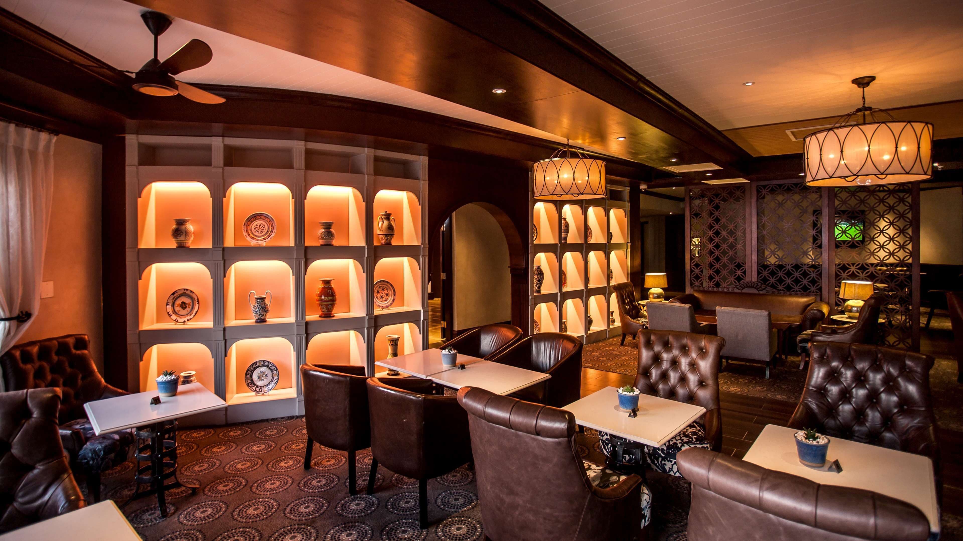 A modern interior with leather seating, tables, and a wall of illuminated shelves displaying decorative items.