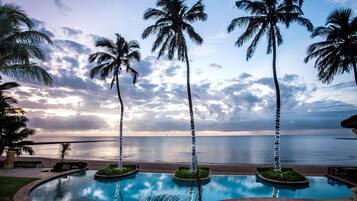 A pool with palm trees and a view of the ocean at sunset.