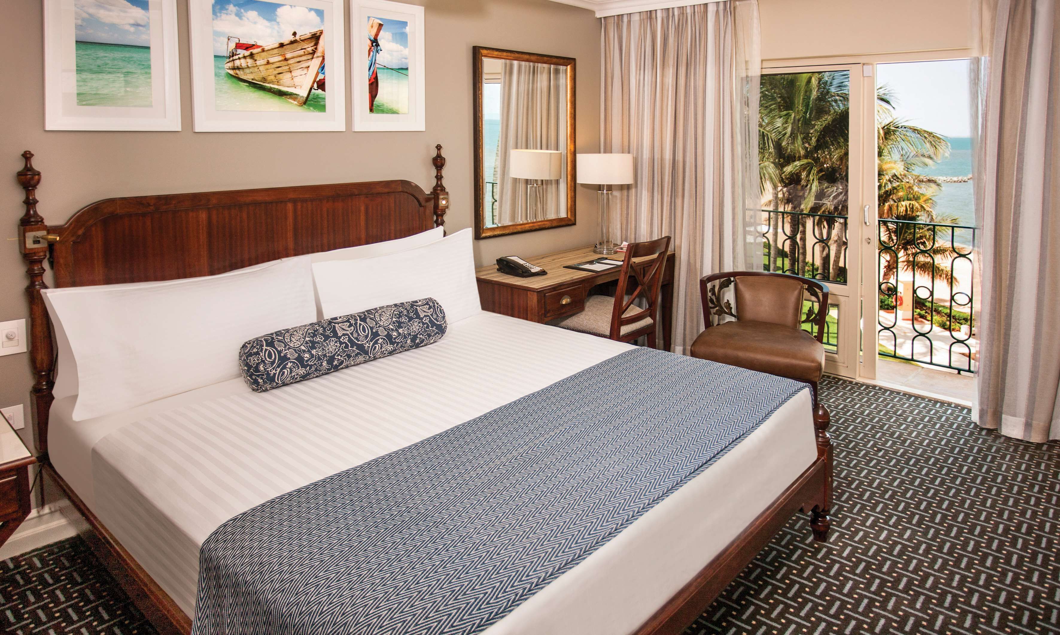 A hotel room with a large bed, a desk, a chair, and a view of the ocean through the window.
