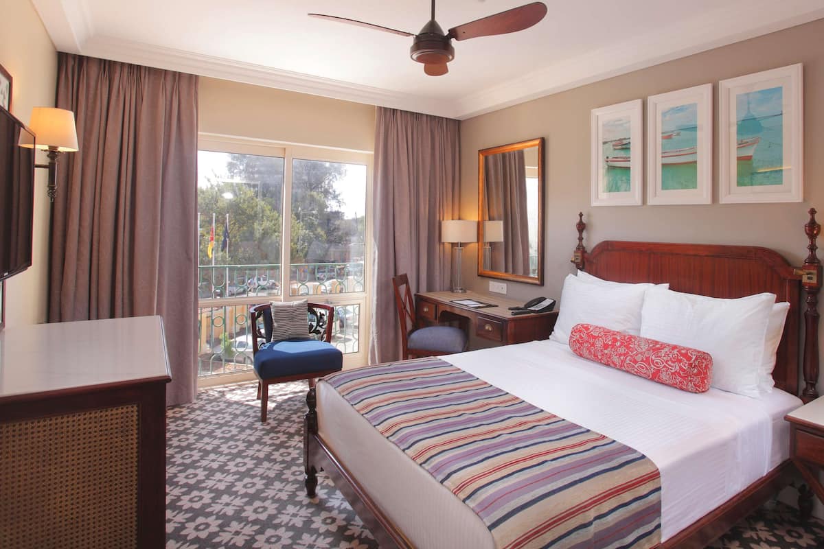 A hotel room with a large bed, a desk, a chair, a balcony view, and artwork on the wall.