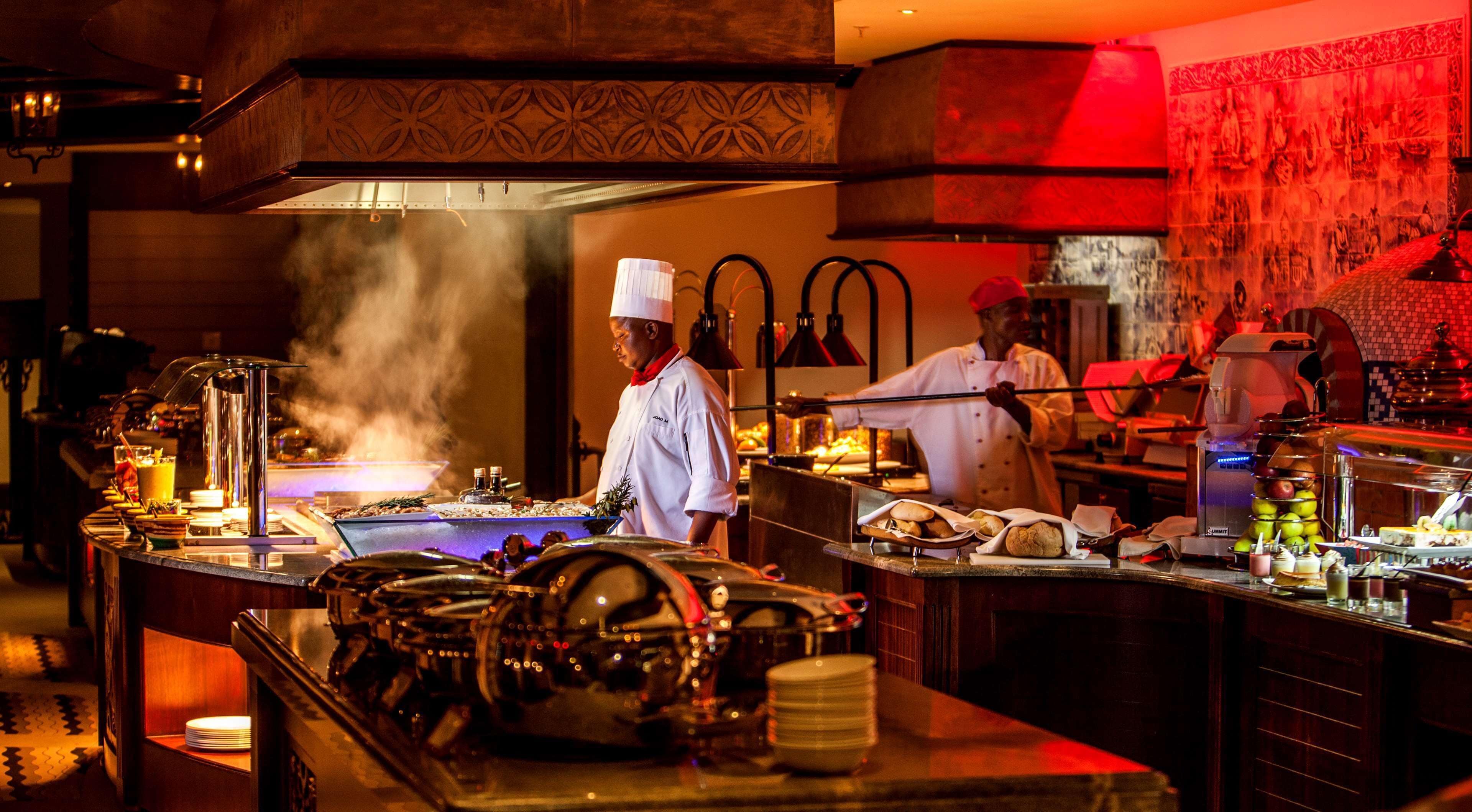 Une cuisine professionnelle où les chefs sont à l’œuvre, équipée d’appareils en acier inoxydable et où une grande variété d’aliments sont exposés.