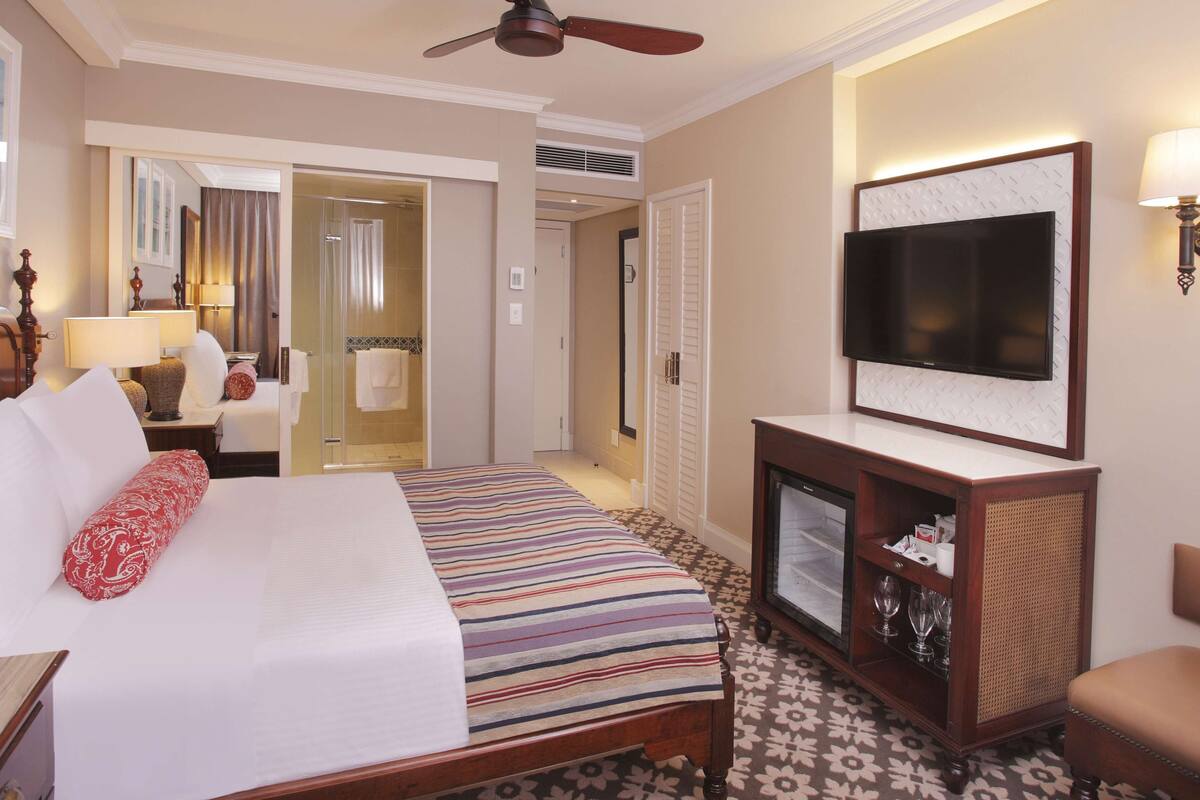 A hotel room with a large bed, a television, a desk with a lamp, and a bathroom visible through an open door.