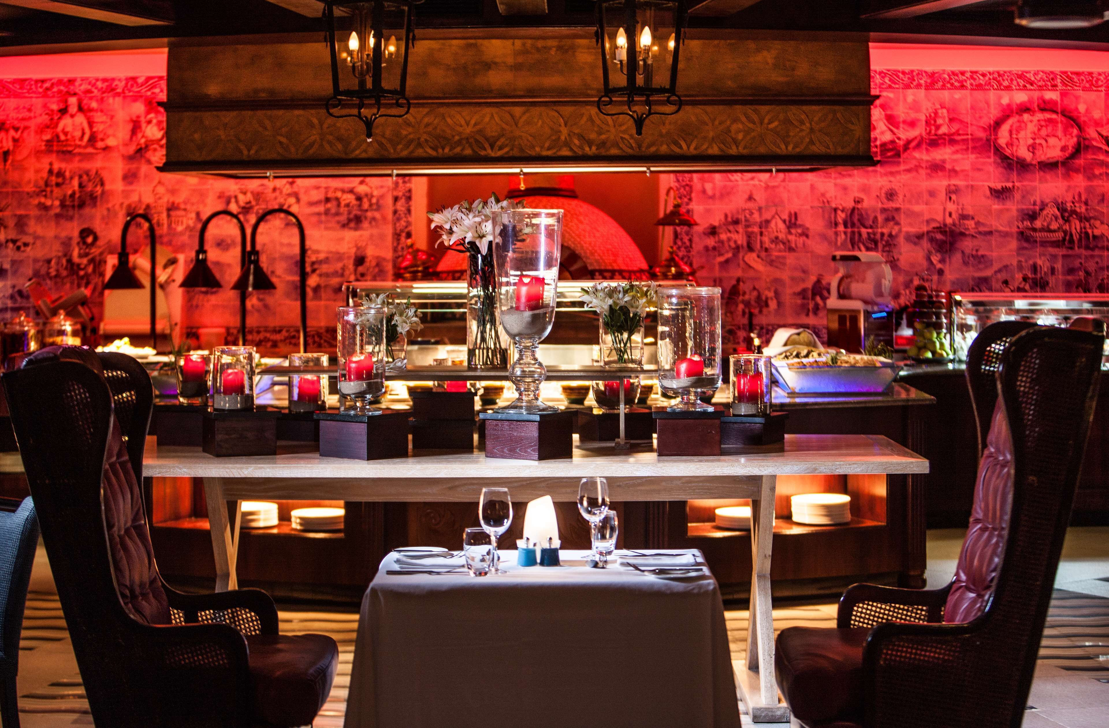 A restaurant with a table set for two, featuring a candle centerpiece, wine glasses, and a vase with flowers.
