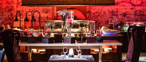 A restaurant with a table set for two, featuring a candle centerpiece, wine glasses, and a vase with flowers.