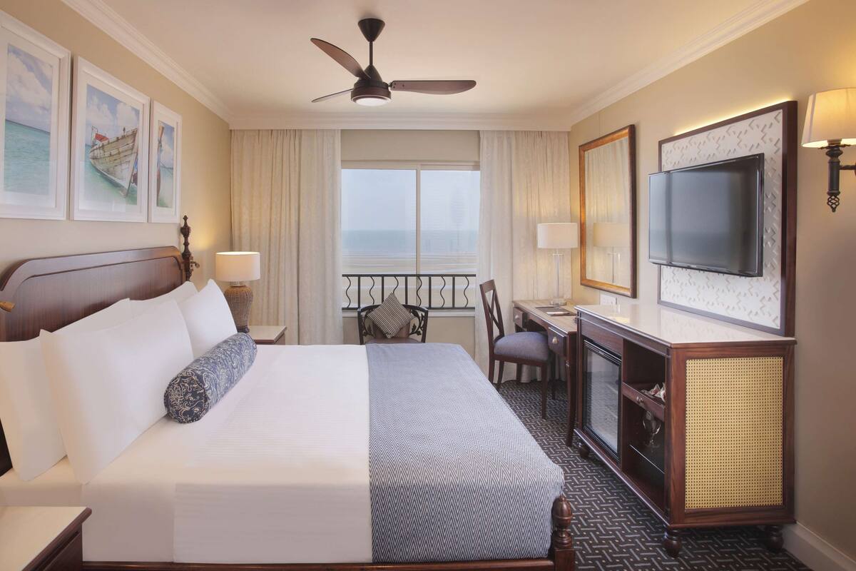 A hotel room with a bed, a desk, a television, and a balcony with a view.