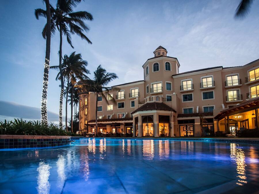 A hotel with a large pool, palm trees, and a well-lit facade.