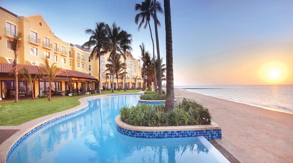 A resort with a swimming pool, palm trees, and a beach view.