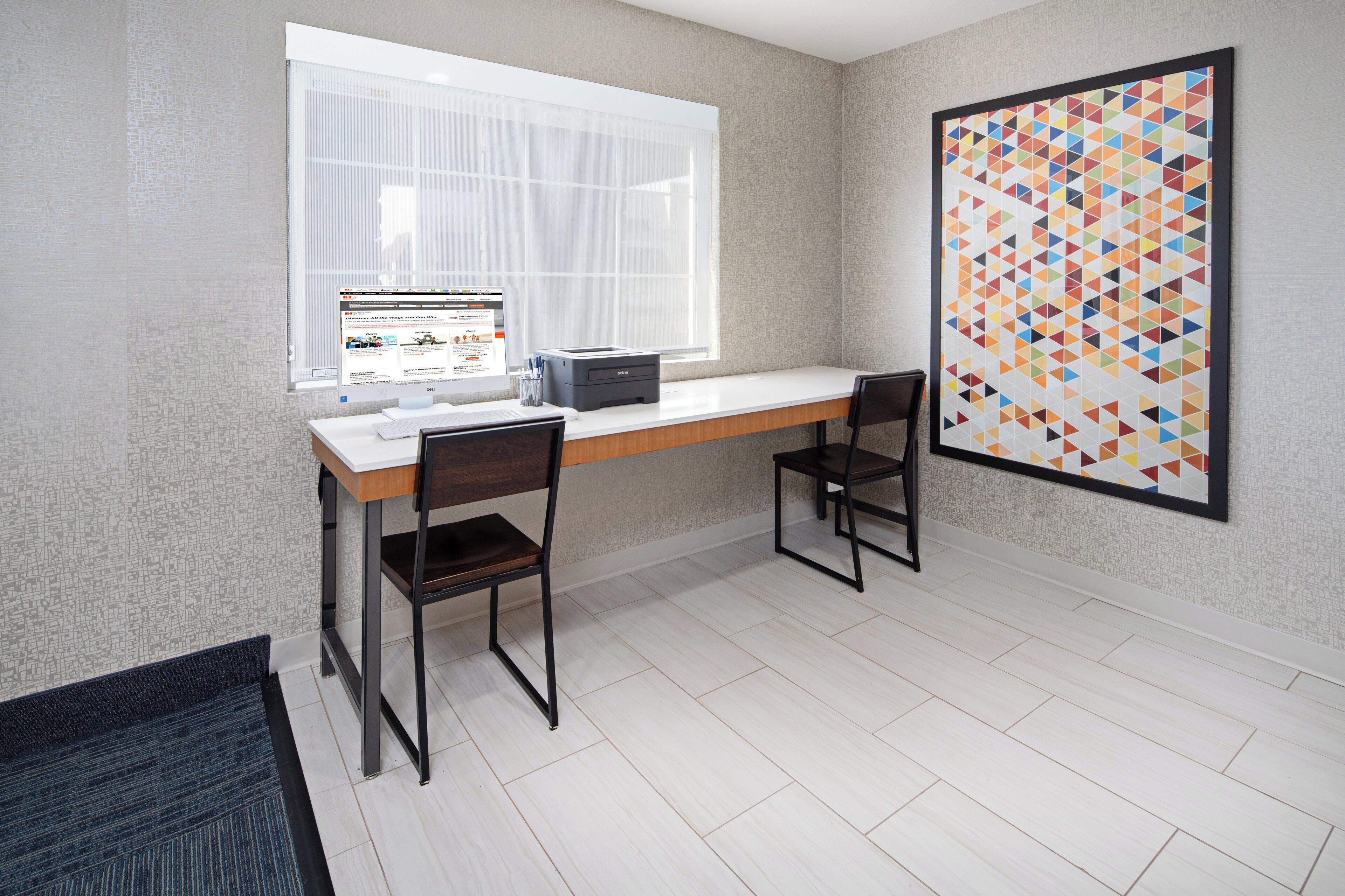 A modern office space with a desk, two chairs, a computer, and a large window.
