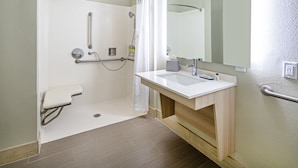 A modern bathroom with a shower, grab bars, a white sink, and a mirror. - Holiday Inn Express & Suites Watsonville by IHG (Watsonville)
