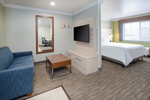A hotel room with a bed, a sofa, a TV, a desk, and a window.