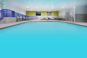 En indendørs swimmingpool med et blåt vandelement, en blå trappe og grønne liggestole.